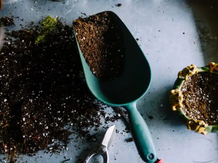 green metal garden shovel filled with brown soil
